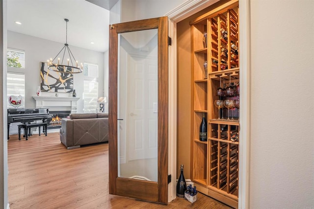 wine area featuring recessed lighting, wood finished floors, a notable chandelier, and a lit fireplace