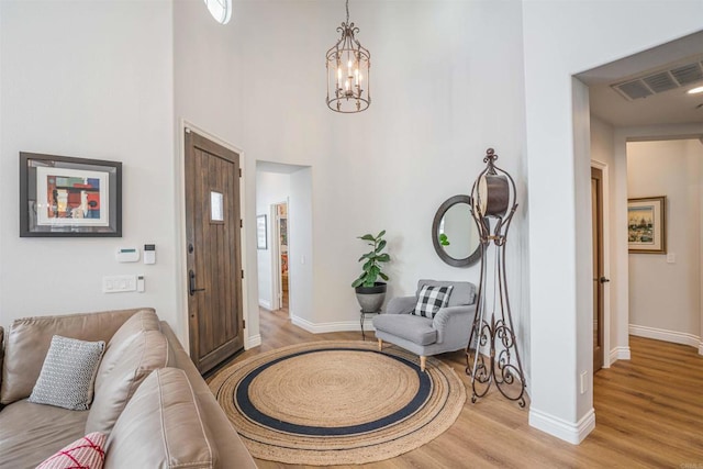 entrance foyer with a chandelier, baseboards, light wood-type flooring, a towering ceiling, and visible vents