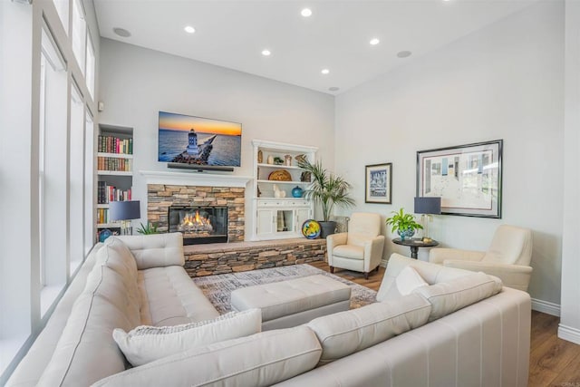 living room featuring built in features, wood finished floors, baseboards, a stone fireplace, and recessed lighting