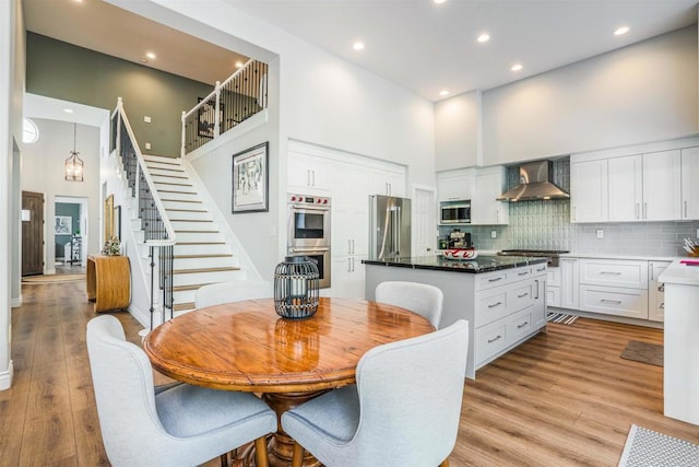dining space with stairs, recessed lighting, light wood-style floors, and a towering ceiling