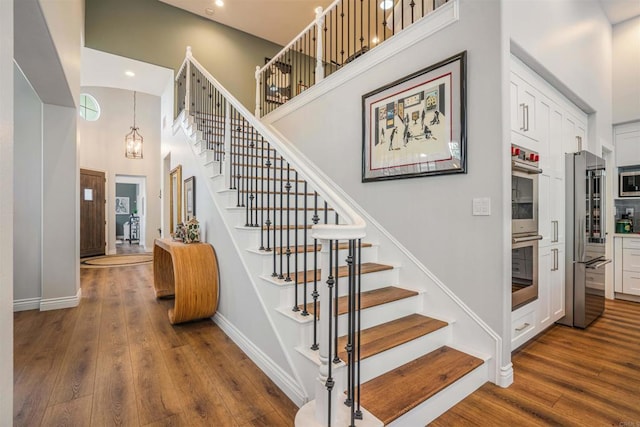 stairs featuring baseboards, recessed lighting, a high ceiling, and wood finished floors