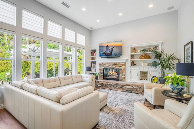 living room featuring a high ceiling, a fireplace, built in shelves, recessed lighting, and visible vents