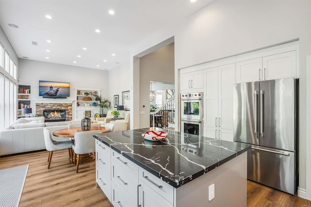 kitchen featuring a stone fireplace, appliances with stainless steel finishes, wood finished floors, recessed lighting, and white cabinetry