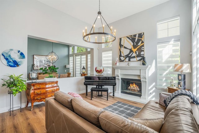 living room featuring an inviting chandelier, baseboards, a glass covered fireplace, and wood finished floors