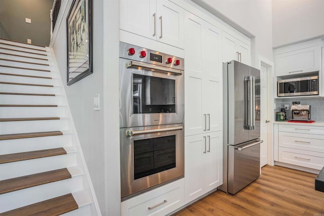 kitchen with white cabinetry, appliances with stainless steel finishes, decorative backsplash, and light wood-style floors