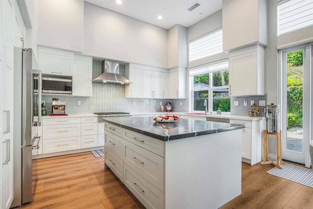 kitchen featuring visible vents, a healthy amount of sunlight, a high ceiling, wall chimney exhaust hood, and stainless steel appliances