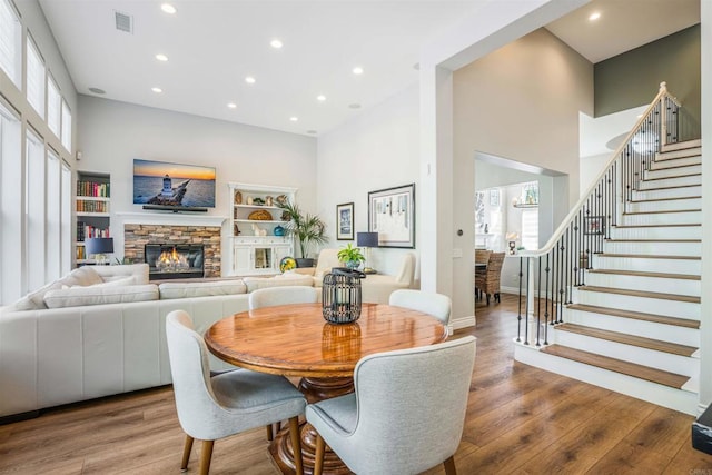 dining space with visible vents, a stone fireplace, wood finished floors, and a towering ceiling