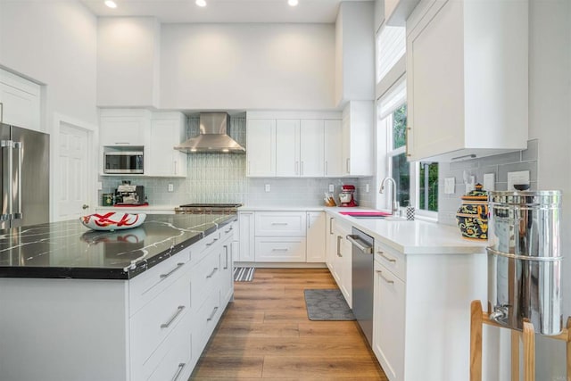 kitchen featuring wall chimney range hood, appliances with stainless steel finishes, decorative backsplash, and a sink