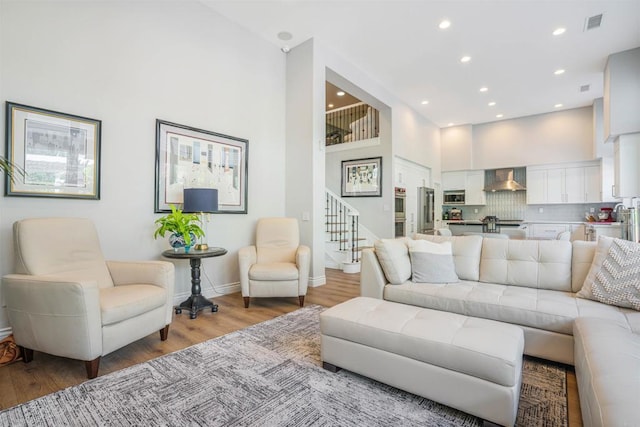 living room with stairs, baseboards, a high ceiling, light wood-type flooring, and recessed lighting