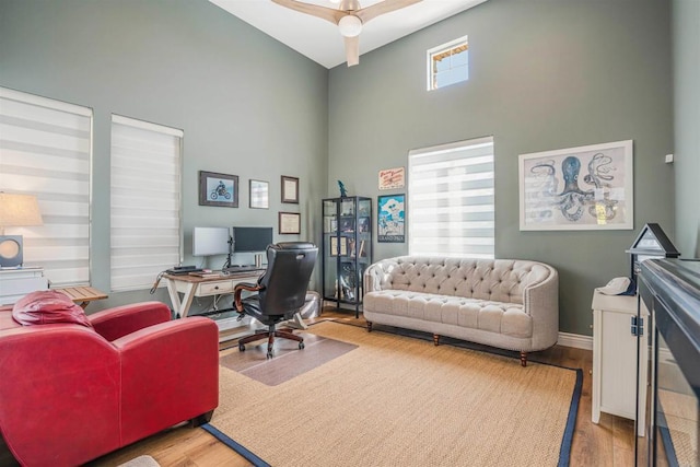 office space with baseboards, ceiling fan, wood finished floors, and a towering ceiling