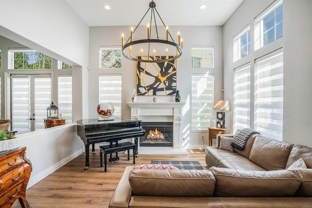 sitting room featuring baseboards, a warm lit fireplace, wood finished floors, and a chandelier
