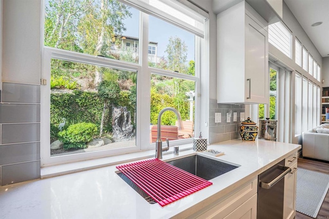 kitchen with decorative backsplash, stainless steel dishwasher, a sink, light countertops, and white cabinets