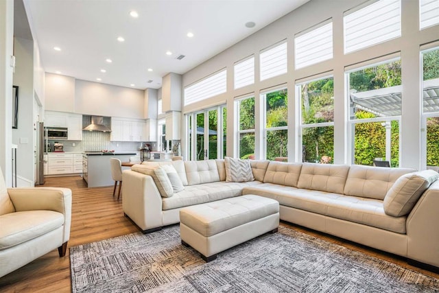 living room with recessed lighting, a towering ceiling, visible vents, and light wood-type flooring
