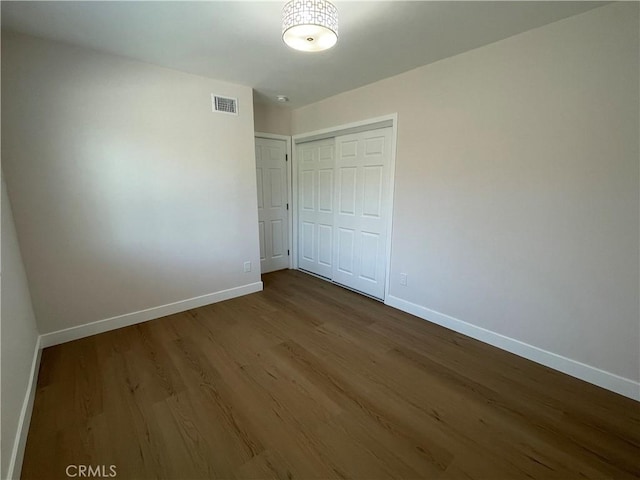 unfurnished bedroom featuring visible vents, a closet, baseboards, and wood finished floors