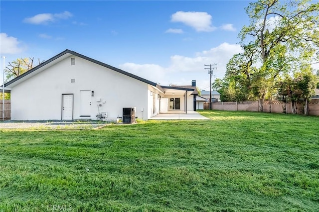 back of property with central air condition unit, stucco siding, fence, and a lawn