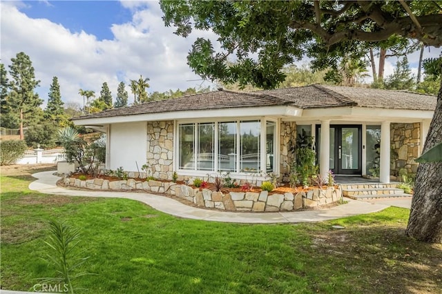 rear view of property with stucco siding, stone siding, and a lawn