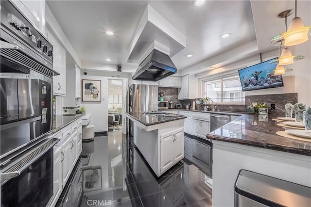 kitchen featuring tasteful backsplash, ventilation hood, white cabinetry, dark stone counters, and stainless steel appliances