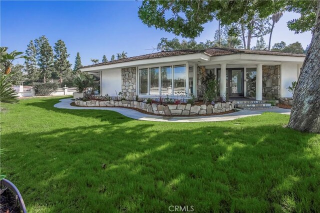back of property featuring stone siding, a lawn, and stucco siding
