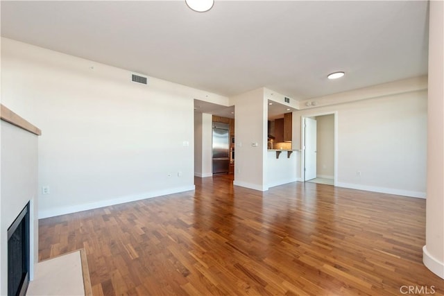 unfurnished living room featuring baseboards, visible vents, wood finished floors, and a fireplace with flush hearth