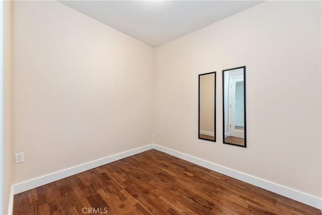 unfurnished room with baseboards and dark wood-type flooring