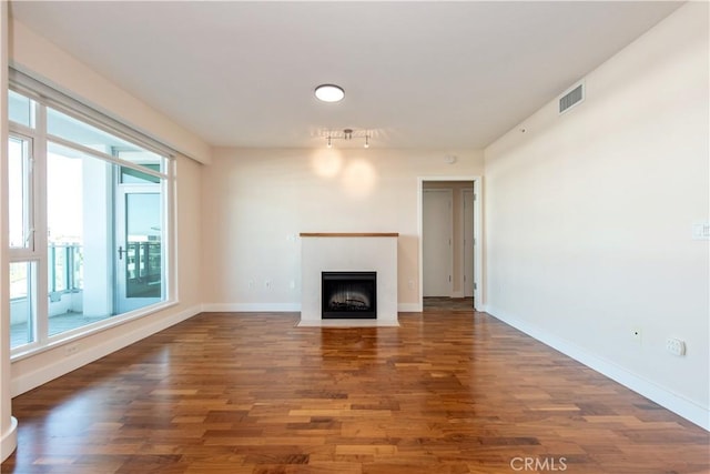 unfurnished living room with baseboards, visible vents, wood finished floors, and a fireplace with flush hearth