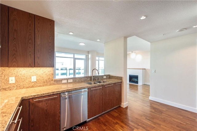 kitchen with backsplash, dishwasher, a fireplace, a sink, and dark wood-type flooring