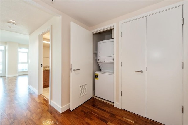 washroom featuring stacked washer and dryer, visible vents, baseboards, wood finished floors, and laundry area