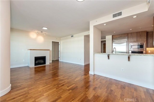 unfurnished living room with a fireplace with flush hearth, wood finished floors, visible vents, and baseboards