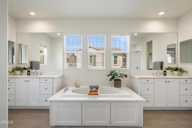 bathroom featuring recessed lighting, plenty of natural light, a garden tub, and a sink