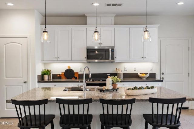 kitchen featuring visible vents, a sink, a breakfast bar, stainless steel microwave, and recessed lighting