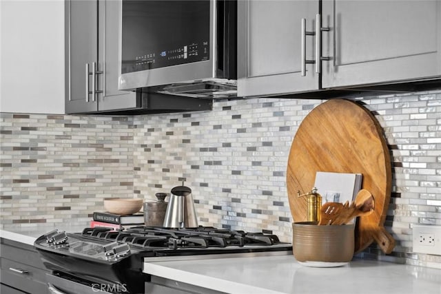 details with stainless steel microwave, gray cabinetry, decorative backsplash, and light countertops