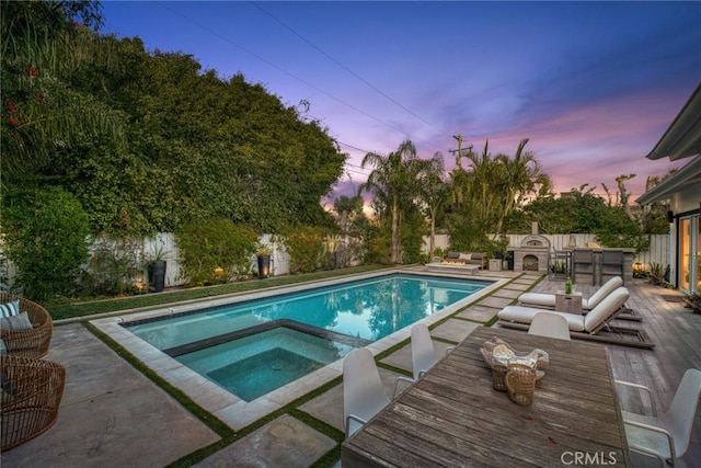 pool at dusk with a patio, a fenced in pool, a fenced backyard, and an in ground hot tub