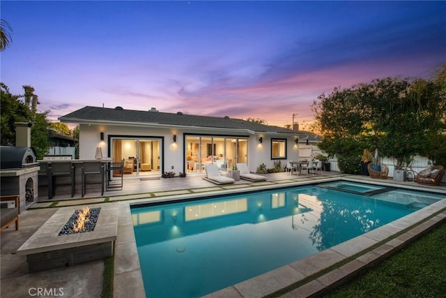 rear view of property with a patio, a bar, an outdoor fire pit, a fenced in pool, and an in ground hot tub