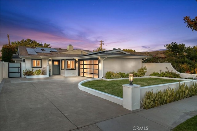 view of front of home with roof mounted solar panels, a front yard, an attached garage, and stucco siding