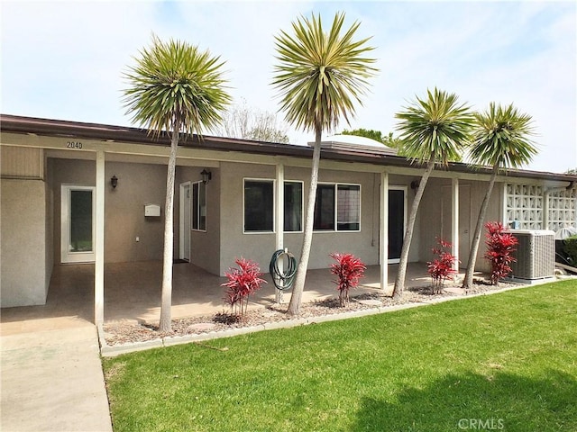 rear view of house featuring stucco siding, a yard, central air condition unit, and a patio