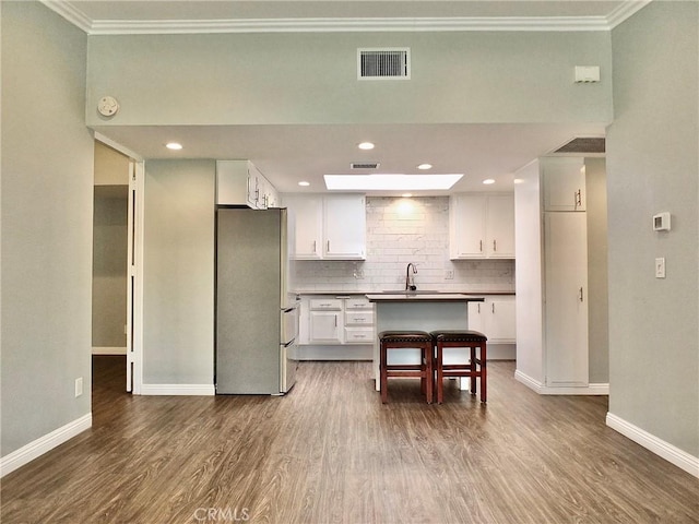 kitchen with backsplash, visible vents, freestanding refrigerator, crown molding, and dark wood-style flooring