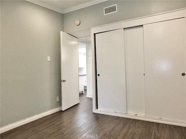 unfurnished bedroom featuring dark wood finished floors, visible vents, ornamental molding, a closet, and baseboards