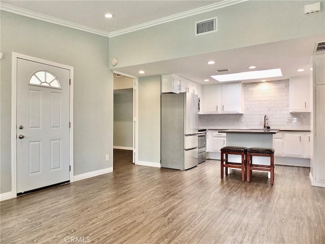 kitchen with crown molding, wood finished floors, white cabinets, backsplash, and appliances with stainless steel finishes