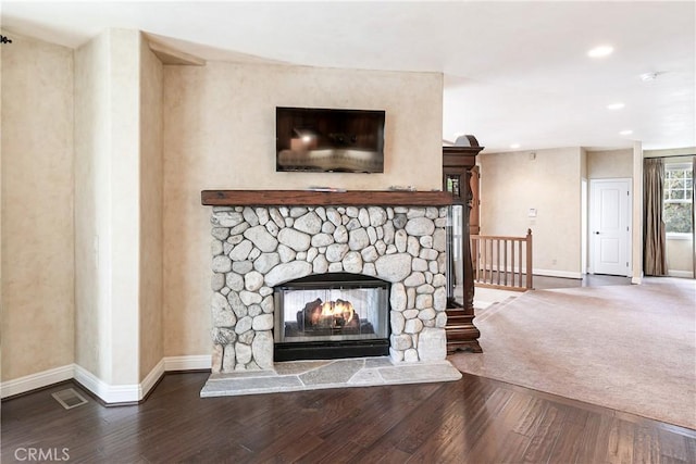 interior space with visible vents, baseboards, a stone fireplace, and wood finished floors