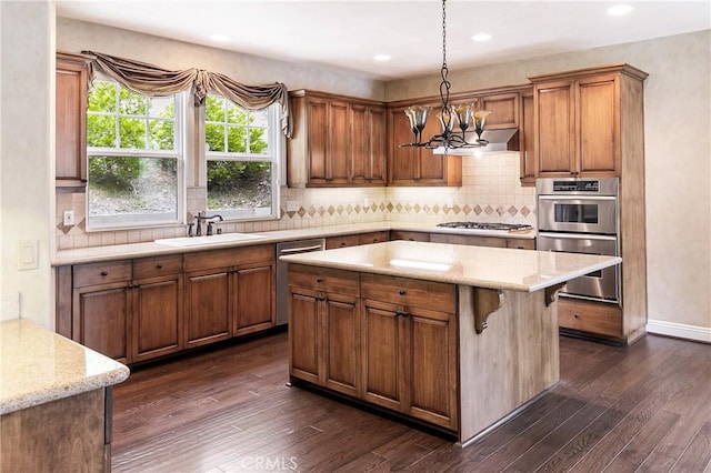 kitchen featuring a sink, dark wood-style flooring, appliances with stainless steel finishes, a chandelier, and brown cabinets