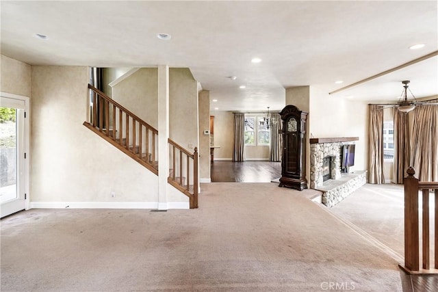 unfurnished living room featuring a stone fireplace, recessed lighting, carpet flooring, and stairs