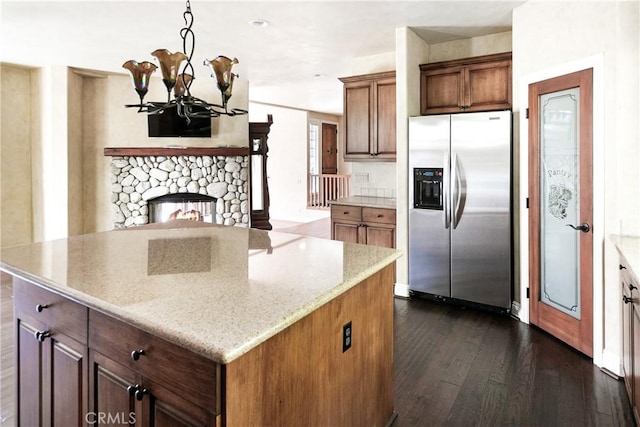 kitchen featuring an inviting chandelier, stainless steel fridge, a center island, light stone countertops, and dark wood-type flooring
