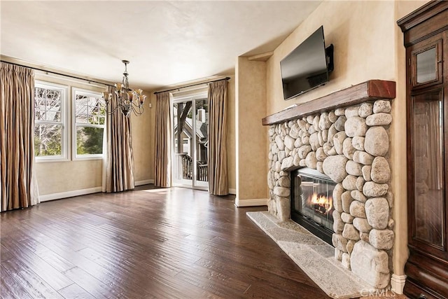 unfurnished living room with baseboards, a notable chandelier, dark wood finished floors, and a stone fireplace