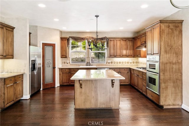 kitchen featuring brown cabinetry, under cabinet range hood, and stainless steel appliances