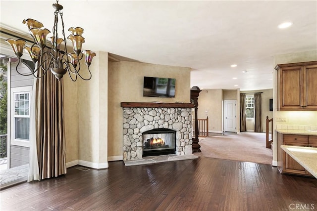 living room with baseboards, an inviting chandelier, dark wood-style flooring, a stone fireplace, and recessed lighting