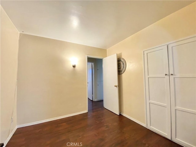 unfurnished room featuring baseboards and dark wood-type flooring