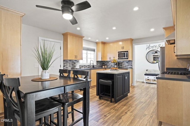 kitchen with stainless steel microwave, light wood-style floors, ceiling fan, a sink, and light brown cabinetry