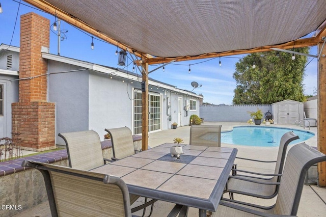 view of patio with a storage shed, a fenced backyard, outdoor dining space, an outdoor structure, and a fenced in pool
