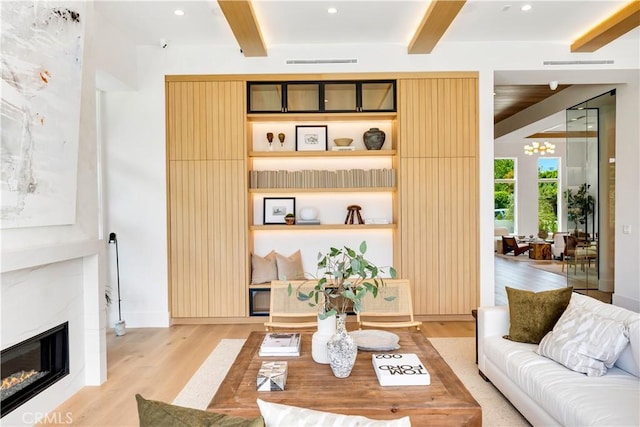 living room featuring a glass covered fireplace, light wood finished floors, visible vents, and beamed ceiling