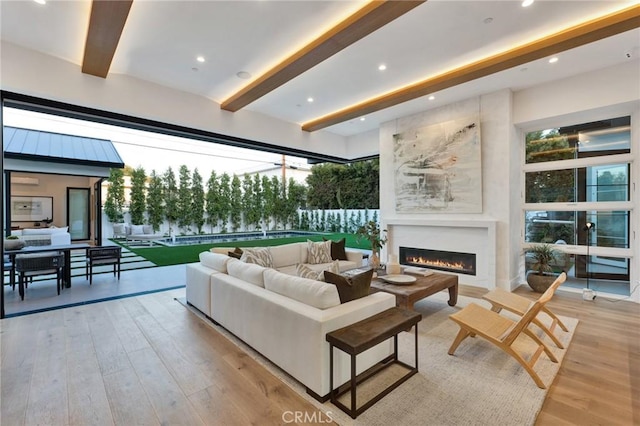 living area with a lit fireplace, light wood-type flooring, beam ceiling, and recessed lighting